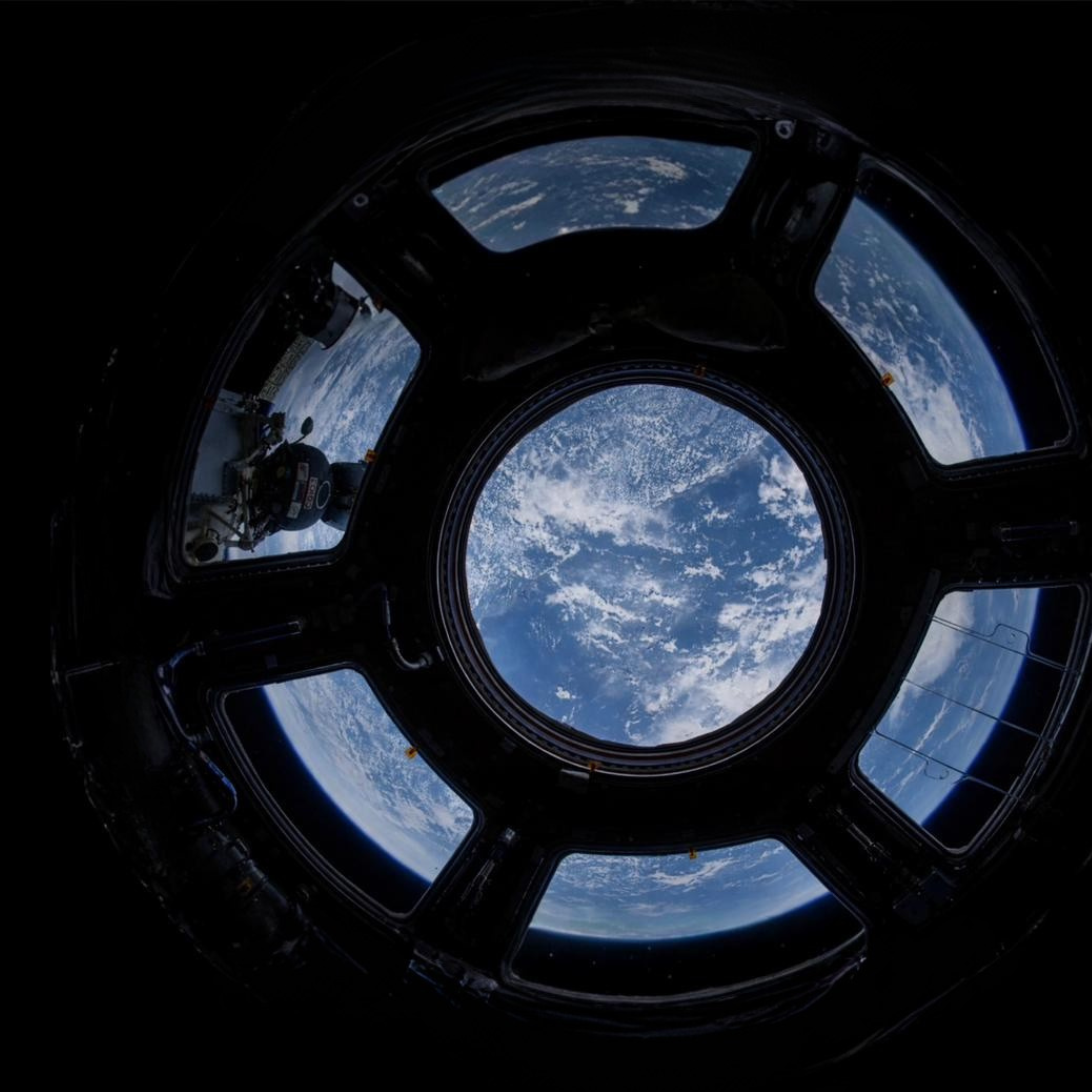 Vista da Terra pelo vitral circular de uma estação espacial, com oceanos e nuvens sobre o planeta.